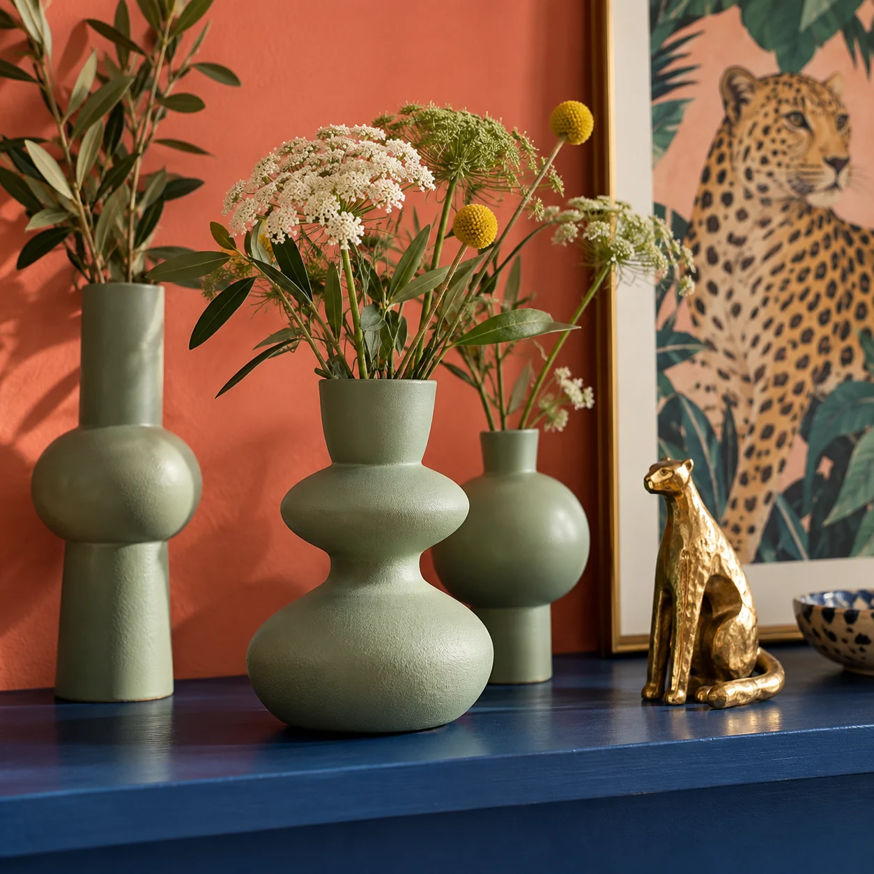 Sage green sculptural vases and a small gold accent on a cobalt shelf.
