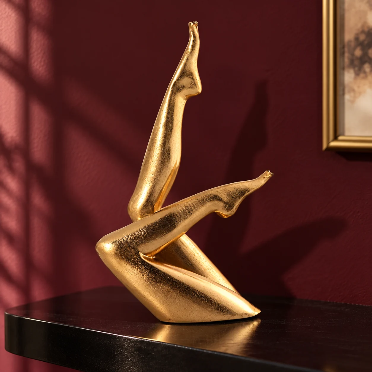 Gold crossed-legs sculpture on a dark shelf against a burgundy wall.