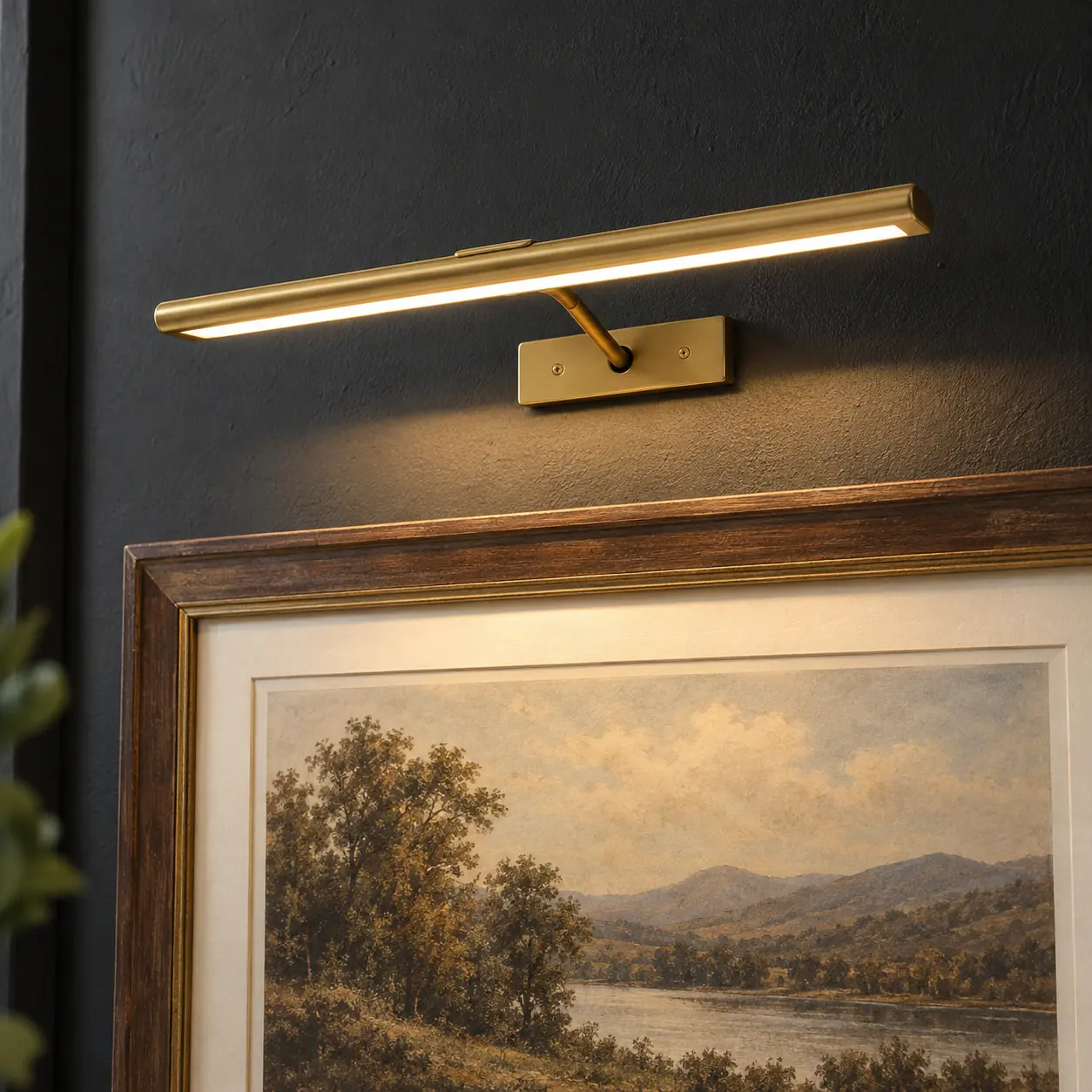 Slim gold picture light illuminating framed artwork on a matte black accent wall