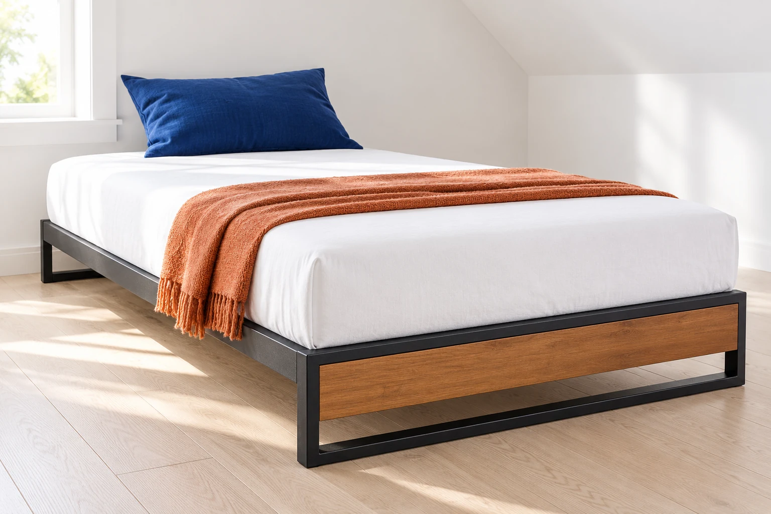 Low platform bed with a black metal frame and wood foot panel in a bright attic bedroom.
