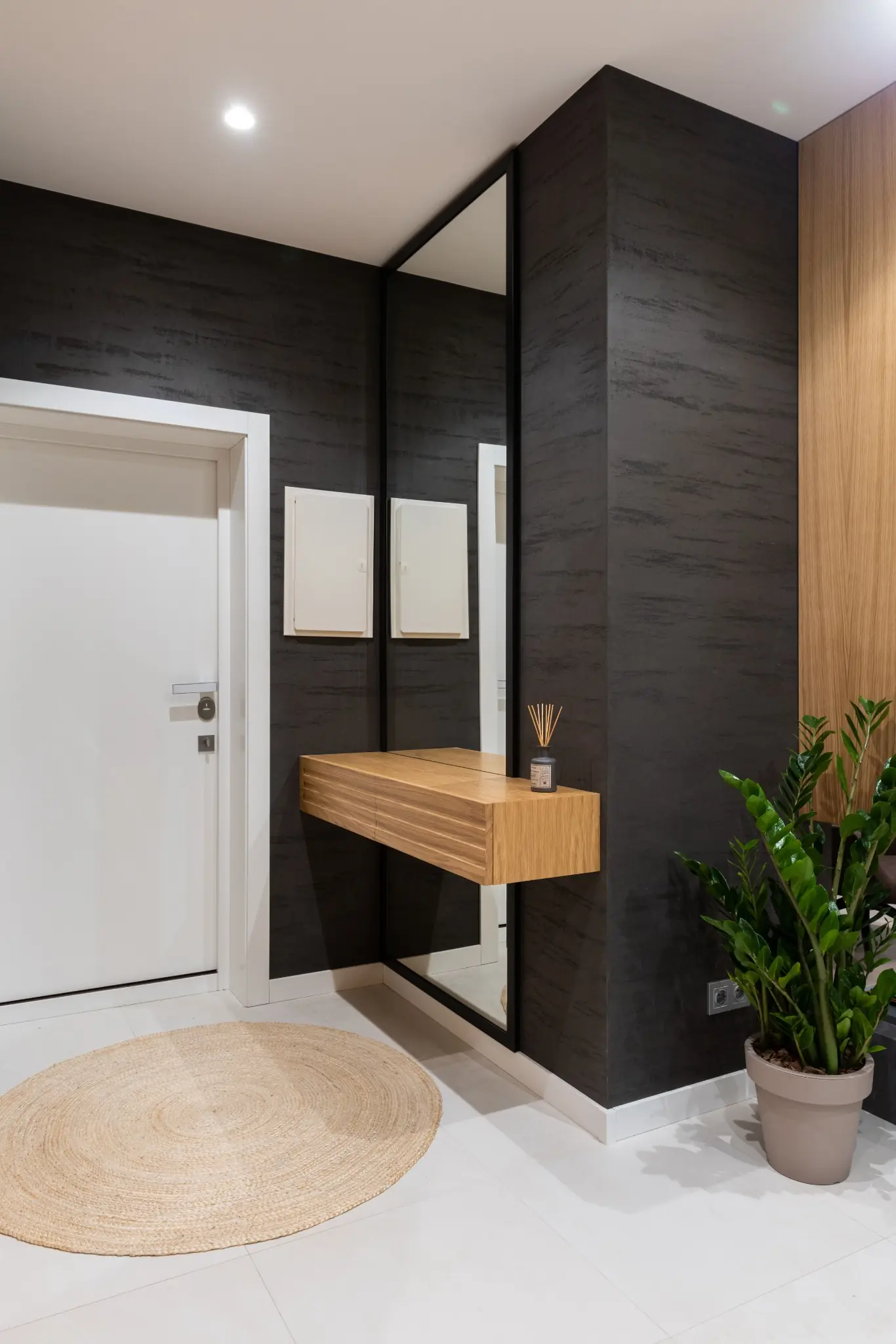 Textured black entryway wall beside a tall mirror and floating wood console